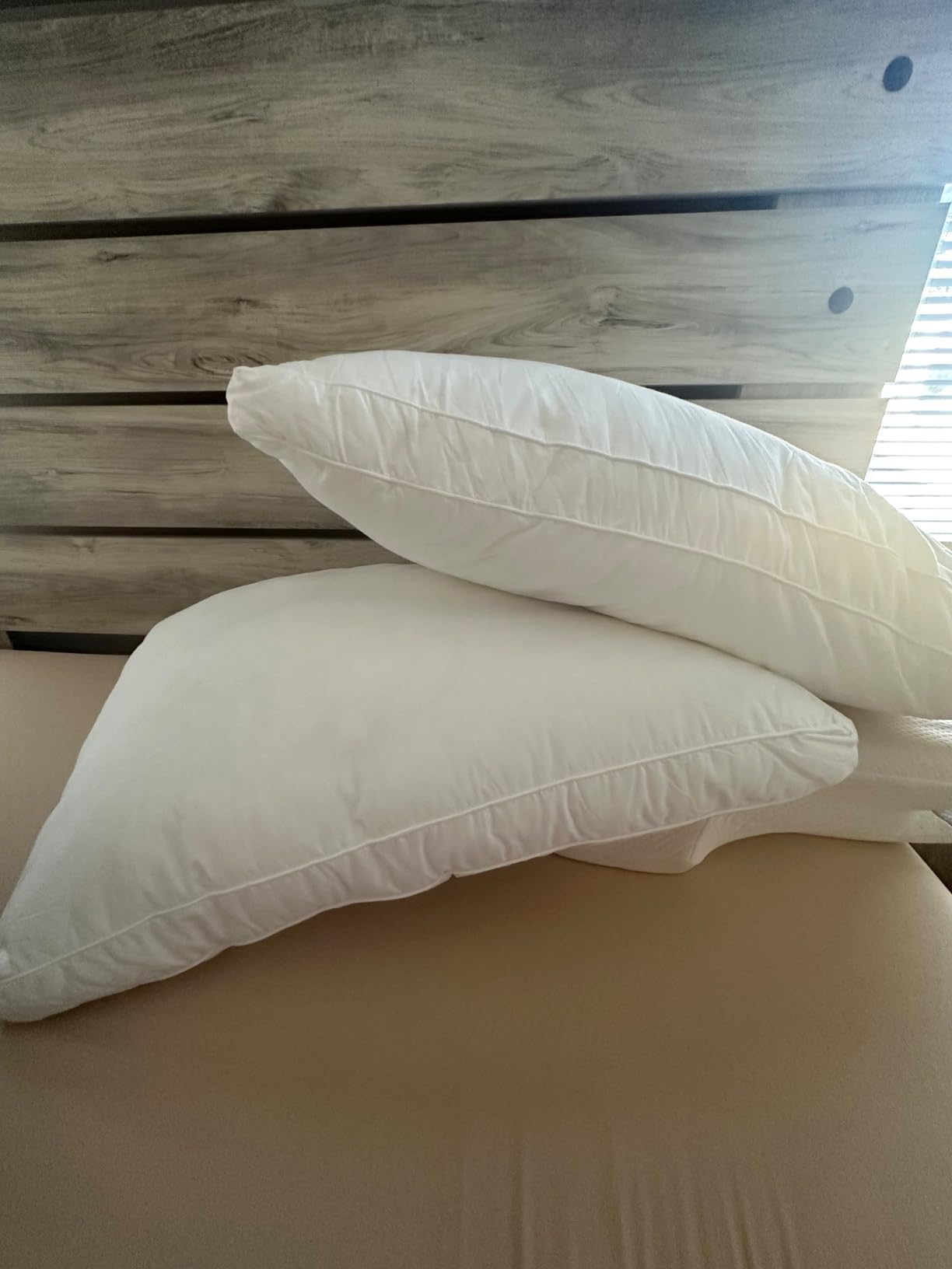 Two white pillows stacked on a bed with a wooden headboard, showing the Utopia Bedding Bed Pillows for Sleeping Queen Size (White) in use for a product review and featured in the 10 Most Recommended Pillows.