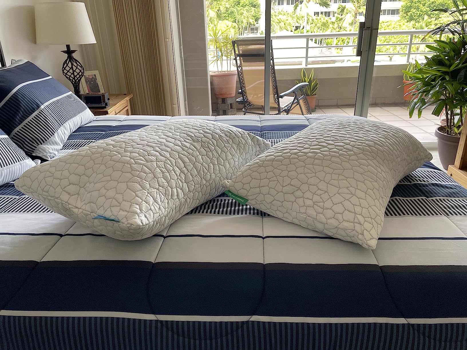 Two Cooling Bed Pillows placed on a bed, with a lovely balcony view visible behind them.