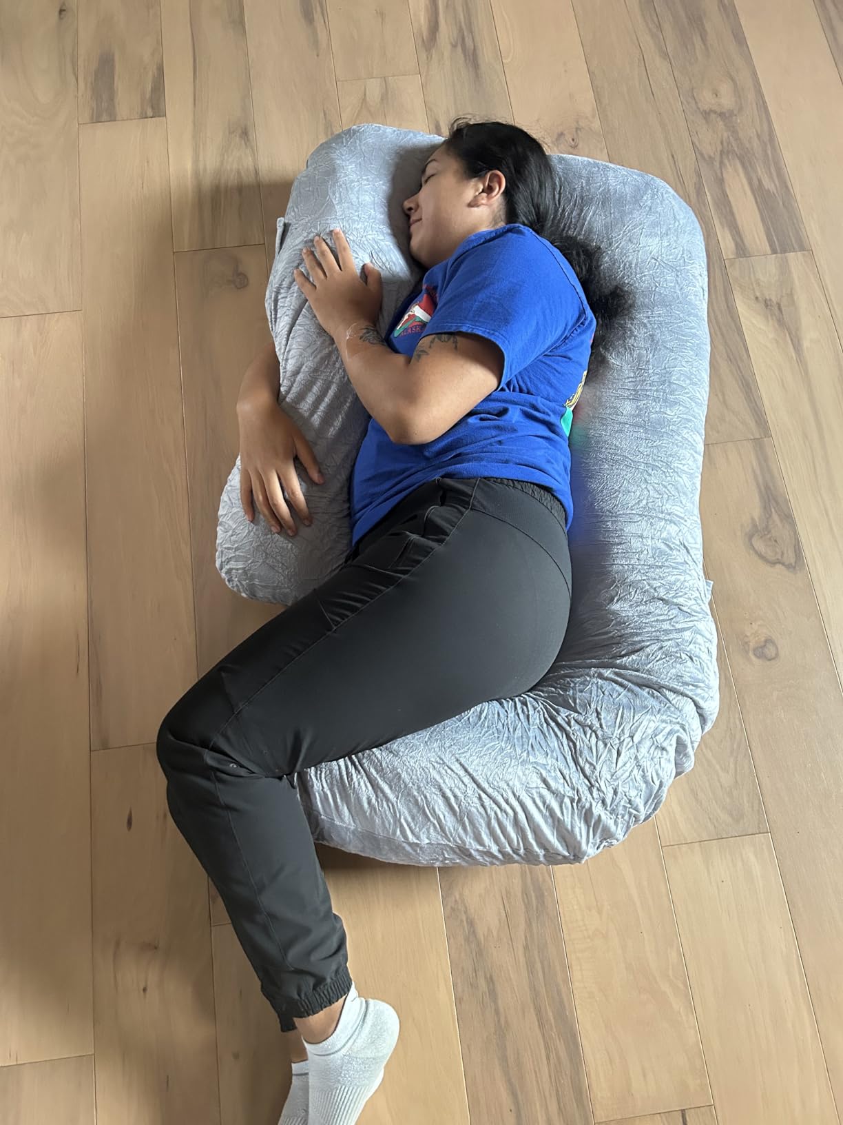 A woman relaxes on a large Pharmedoc Pregnancy Pillow on the floor, enjoying comfort and support. For product review.